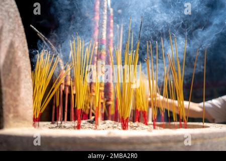 close-up of a hand holding incense. The background is an unspecified, faded temple. Concept of spiritual and religious Stock Photo