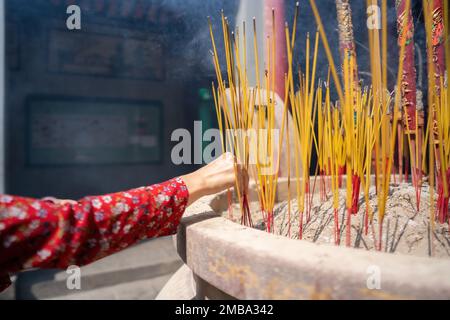 close-up of a hand holding incense. The background is an unspecified, faded temple. Concept of spiritual and religious Stock Photo