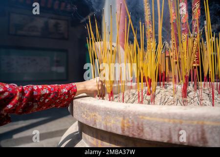 close-up of a hand holding incense. The background is an unspecified, faded temple. Concept of spiritual and religious Stock Photo