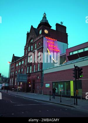 Hornsey Road Baths, Hornsey Road, Finsbury Park, Islington, Greater London Authority, 2012. The entrance block of the former Hornsey Road Baths, Islington, seen from the south at dusk, showing the illuminated neon name sign and figure of a diving woman on the south elevation. The Hornsey Road Baths were built in 1892 and closed in 1991. The swimming pools were demolished and the site redeveloped as Tiltman Place, with blocks of apartments. The entrance block (or gatehouse) and laundry buildings were converted into apartments known as The Gatehouse. The neon sign of a diving woman on the south Stock Photo