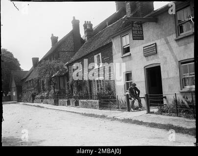 Aylesbury Road, Monks Risborough, Princes Risborough, Wycombe, Buckinghamshire, 1918. Looking south along Aylesbury Road in Monk's Risborough, showing a man in the foreground sitting outside the Nag's Head public house with houses beyond. Since this photograph was taken the pub has closed and is now in use as a house. A sign above the door shows the landlord was George Calcraft and the pub sign shows the pub belonged to Welch Ale Brewery Ltd. Stock Photo