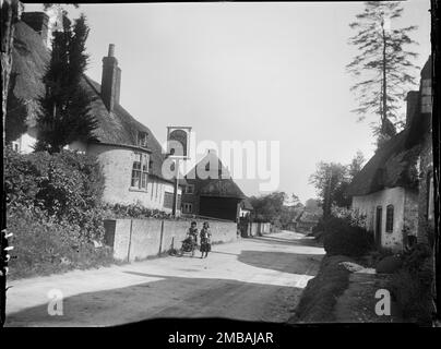 Wootton Rivers, Wiltshire, 1923. A view looking south along the main street through Wootton Rivers, showing The Royal Oak Inn on the left of the foreground and two girls walking past with a young child in a pushchair. Stock Photo