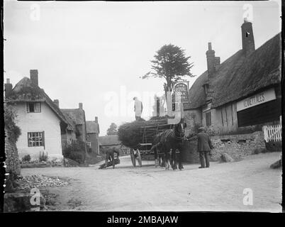 Wootton Rivers, Wiltshire, 1923. A view looking north along the main street through Wootton Rivers, showing three men and a horse-drawn cart laden with coppiced wood outside The Royal Oak Inn. A sign on the front of the pub advertises Kennett Ales. Stock Photo