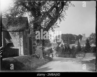 Kingston, Corfe Castle, Purbeck, Dorset, 1927. Looking east from the junction of West Street with South Street in Kingston, showing a boy carrying two buckets away from the village pump and the tower of the Old St James's Church in the distance. Stock Photo