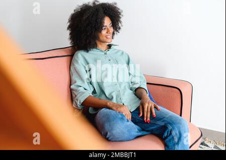 Portrait of carefree young latin woman sitting on the sofa and looking aside. Serene multiracial woman in casual clothes in relaxed atmosphere spending leisure at home Stock Photo