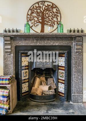 Victorian fossil limestone fireplace surround with black ornate cast iron fireplace and grate with ceramic tiles and split wood logs Stock Photo