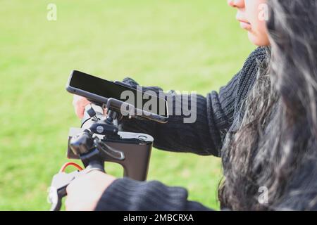 young latina woman, riding an electric scooter and using smart phone app Stock Photo