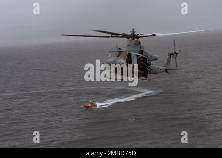 A U.S. Marine UH-1Y Huey helicopter approaches USS Miguel Keith (ESB-5) while a 7-man Rigid Hull, Inflatable Boat, manned by Expeditionary Operations Training Group members prepare to insert Marines conducting visit, board, search, and seizure operation off the coast of Okinawa, Japan, June 14, 2022. Inserting from both air and sea allows the Marine Amphibious Raid Force and Battalion Landing Team 2/5 security team to quickly seize the key areas of the ship. The 31st MEU, the Marine Corps' only continuously forward-deployed MEU, provides a flexible and lethal force ready to perform a wide rang Stock Photo