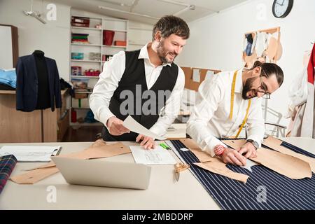 Young tailor working in atelier monitored by his coworker Stock Photo