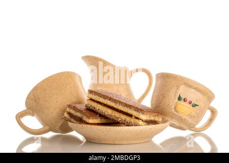 Two mini cocoa sponge cake on ceramic saucer with two cups and milk jug, macro isolated on white background. Stock Photo