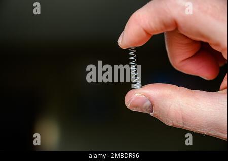 Caucasian hand compressing a metal spring between a thumb and finger ...