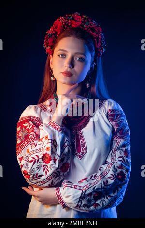Ukrainian pretty woman in traditional necklaces and embroidered ethnic blouse at blue smoke background. Ukraine, style, folk, culture. Stock Photo