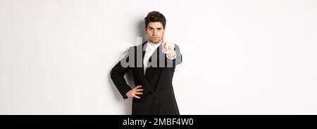 Portrait of serious handsome man in business suit, showing one finger to prohibit or decline something, telling to stop, disagree with you, standing Stock Photo