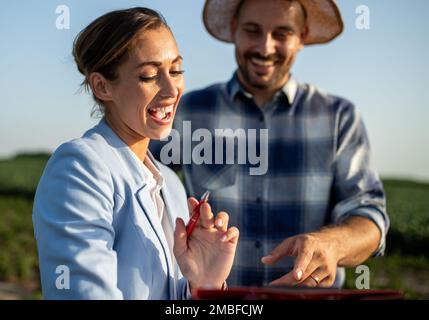 Pretty business woman and handsome farmer signing documents on field in summer time Stock Photo
