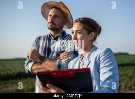 Pretty business woman and handsome farmer standing in field in summer Stock Photo