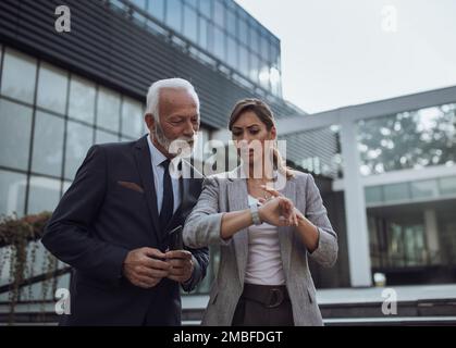 Senior businessman and young woman talking in hurry in front of office building Stock Photo