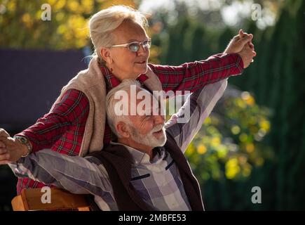 Senior woman holding spread hands of mature man behind him in park Stock Photo
