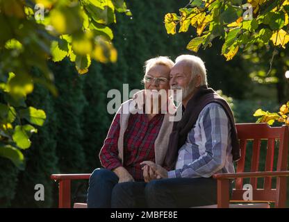 Cute senior couple sitting in hug on bench in park Stock Photo