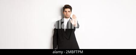 Portrait of serious handsome man in formal suit, extending hand to stop you, prohibit action, forbid and disagree with something, standing against Stock Photo