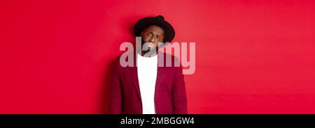 Sad and unamused Black man looking with pity at camera, frowning disappointed, standing against red background Stock Photo