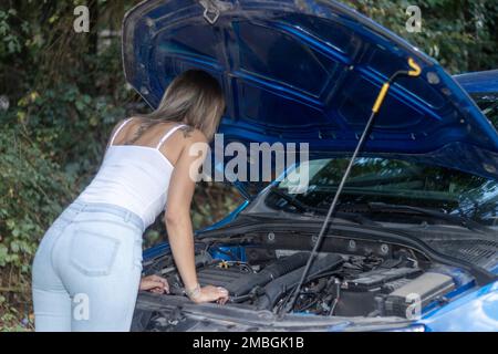 woman standing near a parked broken down car having trouble with her vehicle. Woman driver waiting for help besides auto malfunction Stock Photo