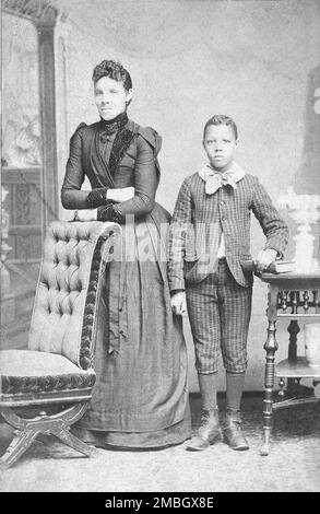 Unidentified standing figures: woman, her folded arms leaning on back of chair, and young man, probably her son, left hand on book, c1890. Additional title: Domestic life Stock Photo