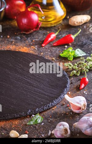 Culinary background with kitchen slate round board, olive oil in a jug and vegetables. Empty space for menu or recipe with selective focus Stock Photo