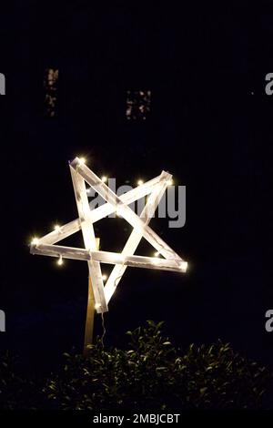 Star light up at night with bush below and darkened building in the background.  Star is more towards the bottom, left portion. Stock Photo