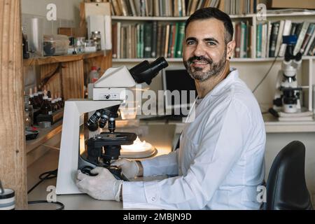 Scientist in front of microscope, smiling and looking at camera. Stock Photo