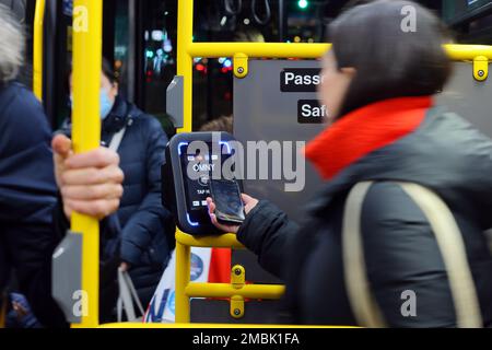 A person taps a smartphone to an OMNY contactless payment reader on a NYC Transit bus. The reader accepts EMV payments through NFC Stock Photo