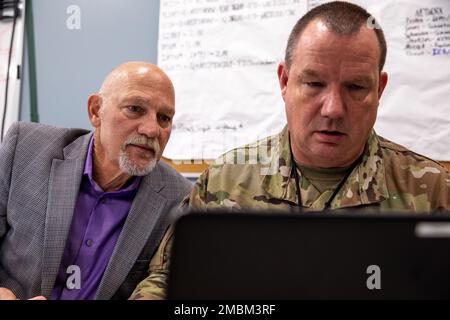 Richard Dumont, left, a network manager assigned to the Rhode Island Army National Guard, looks over at the computer screen of U.S. Air Force Master Sgt. Richard Schneider, Client Support, 158th Fighter Wing, Vermont Air National Guard at Camp Nett, Niantic, Connecticut, June 16, 2022. Soldiers, airmen and Department of Defense civilians from across New England worked together as network defenders (blue teams) in order to repulse a simulated cyber attack from a network intruder (red team). Stock Photo