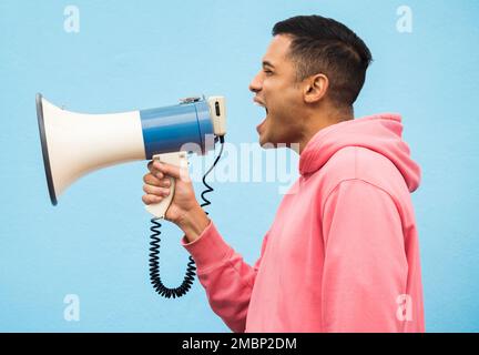 Man, speaker and megaphone in studio for justice, microphone speech and communication in blue background. Male shouting, protest announcement and Stock Photo