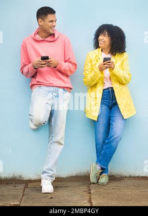 Happy friends, phone and smile leaning on a wall enjoying social media, conversation or communication in the outdoors. Man and woman smiling for Stock Photo