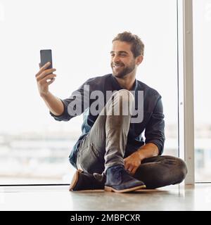 Just resting along the journey to success. Full length shot of a handsome young businessman sitting in an airport terminal and taking a selfie with Stock Photo