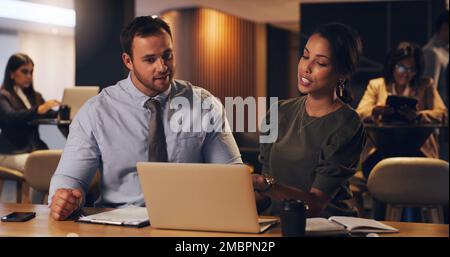 Working through all their plans in detail. two businesspeople working together on a laptop in an office at night. Stock Photo