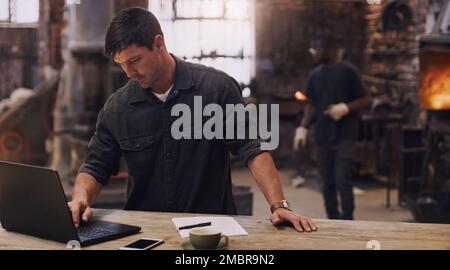 Any business comes with admin that needs to be done. a man using his laptop while working in a workshop. Stock Photo
