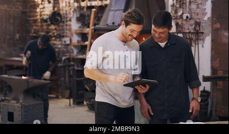 We were mentioned by the biggest mogul in the industry. two men discussing something on a digital tablet while in their workshop. Stock Photo