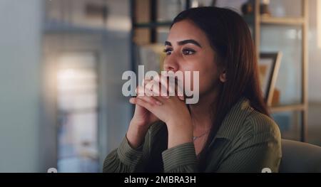 Reading through it all very carefully. a young businesswoman looking thoughtful while working on a computer in an office at night. Stock Photo