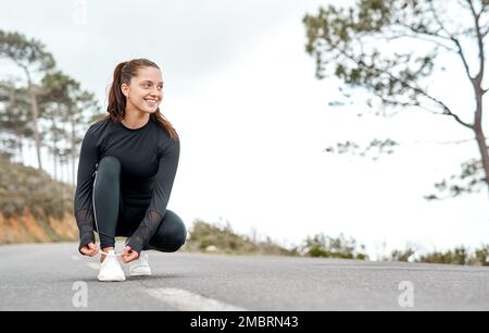 You have to work for the body you want. Full length shot of an attractive young woman tying her shoelaces before exercising outdoors alone. Stock Photo