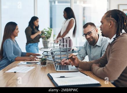 Youre doing great with this task. two handsome businessmen sitting and using a laptop in the office while their colleagues work around them. Stock Photo