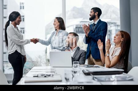 This merger will lead to plenty of positive results. a group of businesspeople applauding their colleagues in an office. Stock Photo