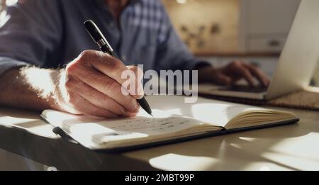 I take notes because my age makes me forget. an unrecognizable man sitting alone in the kitchen at home and working from home. Stock Photo