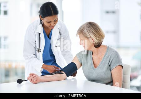 Dont leave it before its too late. a young doctor examining a senior woman with a blood pressure gauge. Stock Photo