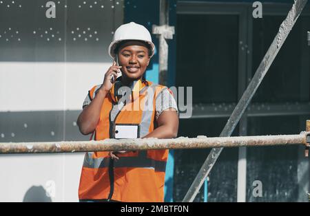 Alls going well on the new build. a young woman talking on a cellphone while working at a construction site. Stock Photo