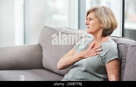 Chest pain is a cause for concern. a senior woman suffering from chest pain while sitting on the sofa at home. Stock Photo