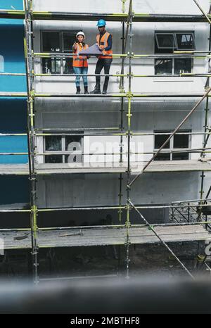 Building commitment within their team. a young man and woman going over building plans at a construction site. Stock Photo