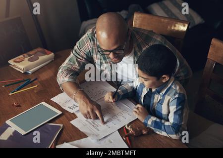 What we learn from dad, well never outgrow. an adorable little boy using a digital tablet while completing a school assignment with his father at home Stock Photo