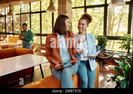 Two young business woman enjoying pleasant conversation in coworking space Stock Photo