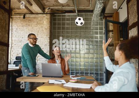 Young diverse multiethnic colleagues playing football in coworking office Stock Photo