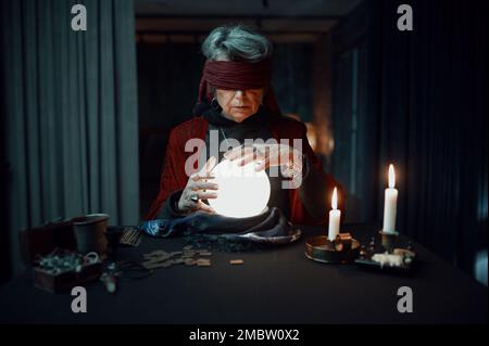 Blindfolded fortune teller using glowing crystal ball for future reading Stock Photo